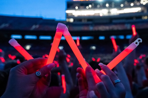 Hands holding up glow sticks in the shape of a W.
